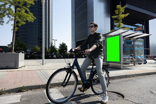 young businessman rides e-bike on his way to the tower where his office is located
