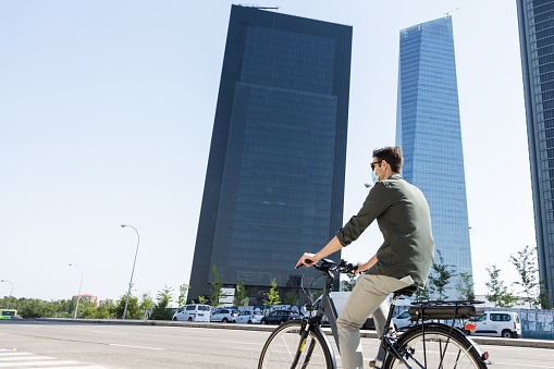 young businessman rides e-bike on his way to the tower where his office is located