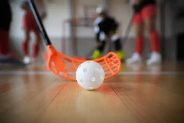Close-up of floorball stick and ball during woman floorball match in a gym.
