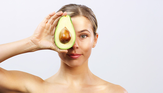 Woman with avocado, glowing skin happy for skincare and nutrition of eating as food. Girl has fresh healthy fruit over face, to use as organic face mask to help for beauty and wellness.