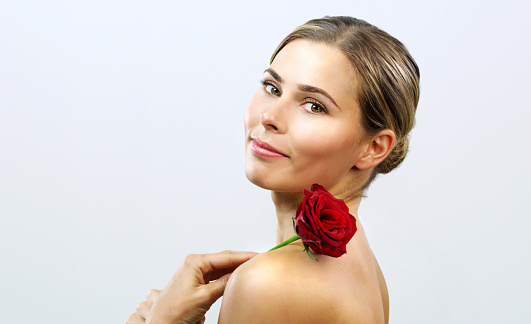 Attractive blonde lady with roses and peonies in her bra touching her face and looking at camera with serious expression