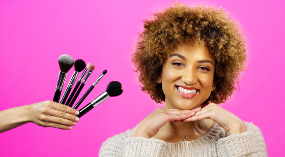 A young Caucasian woman is sitting at her table and applying blush to he cheeks.