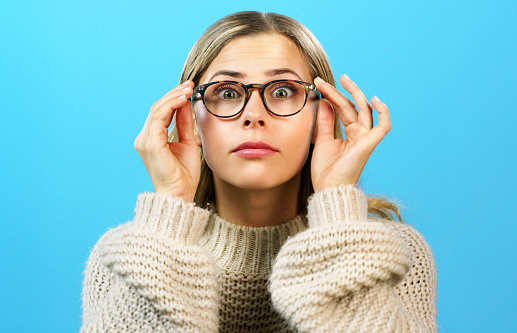 Woman, nerd or geek with glasses for vision and eyesight against a blue studio background. Female with prescription or insurance eyes lenses, eyewear or spectacles to see better and clear sight