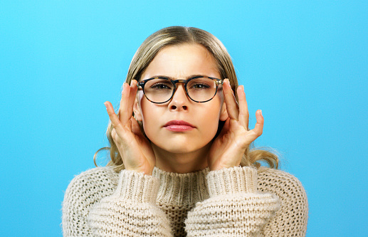 Vision, sight and a woman with glasses squinting at the view on a blue background. Poor eyesight, eye health and cute frames, young girl needs lens update. Focus, squint and try to see with bad eyes