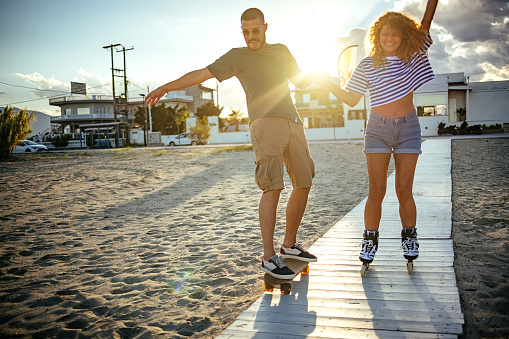 Young couple is rollerblading and skateboarding on the beach