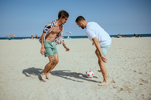 Two young man playing soccer on the beach