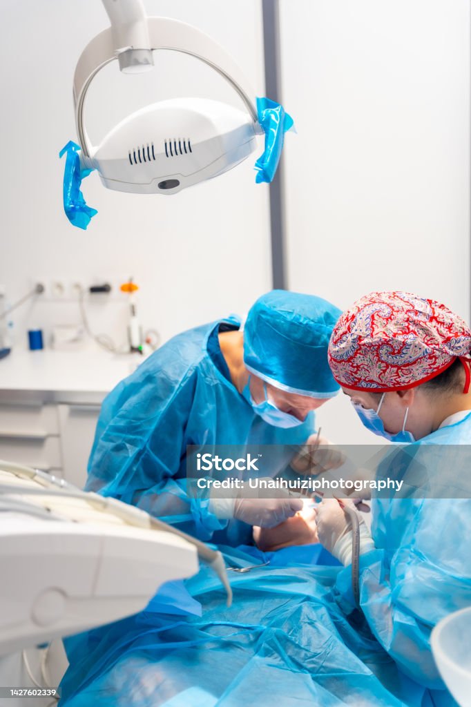 Weibliche Zahnärzte in blauen Peelings, die eine komplizierte Operation an einer weiblichen Patientin durchführen und Blut saugen - Lizenzfrei Arzt Stock-Foto