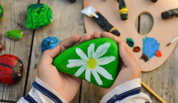istock Outdoor workshop in summer. A selective focus of a schoolboy boy holding a painted flat stone in his hands. Do it yourself. 1427609821