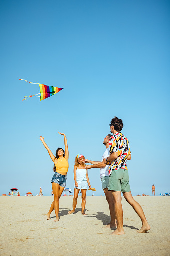 Group of young people playing with a kite on beach in sand outdoors in summer