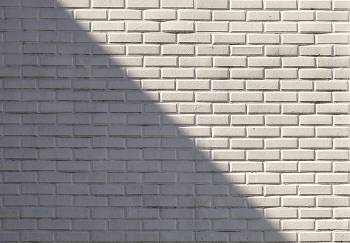 White painted brick wall divided in two by a shadow. Background and texture. Copy space.