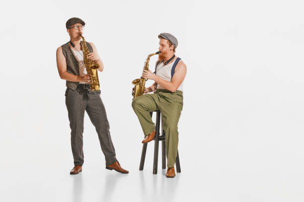 istock Two young musicians in retro style clothes playing saxophones isolated over white studio background. Concept of music, hobby, festival. 1427615297