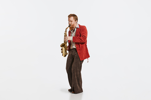 Timeless blues. Young musician in retro style outfit playing saxophone isolated over white studio background. Concept of music, hobby, festival.