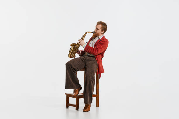 istock Young musician in retro style outfit playing saxophone isolated over white studio background. Concept of music, hobby, festival. 1427615364