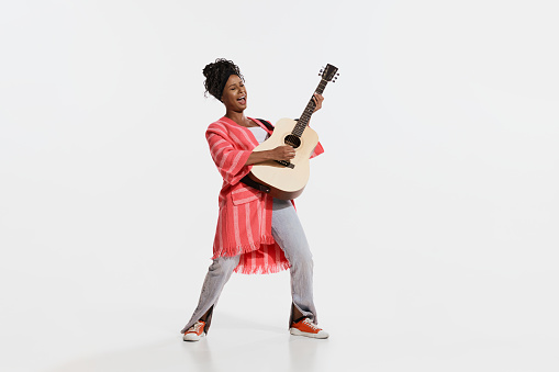 Solo. Stylish african woman wearing vintage style bright clothes playing guitar isolated on white background. Vintage fashion, music, art, emotions, music festival concept.