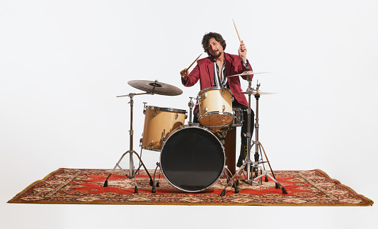Music, beats, atmosphere. Young musician with drums performing over white background. Concept of music, hobby, festival, entertainment Joyful, inspired drummer.