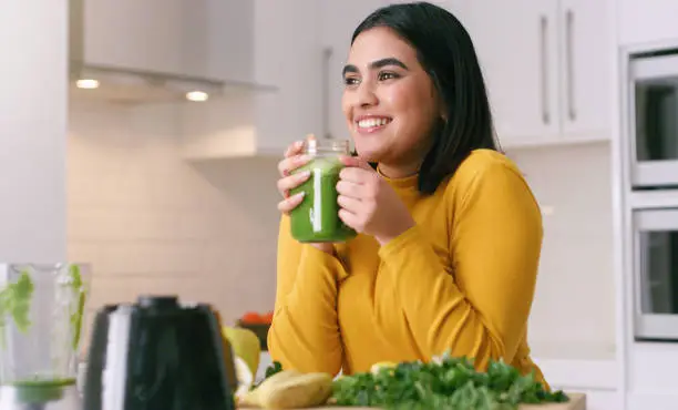 Photo of Banana, spinach and woman with a healthy smoothie for protein, green vegetables and energy in home kitchen. Fruit, smile and happy girl drinking organic detox juice for her vegan diet from blender