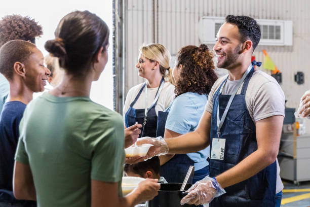 Cheerful, diverse volunteers serve hungry in soup kitchen A cheerful, multiracial group of volunteers serve the hungry at the food bank soup kitchen. altruism stock pictures, royalty-free photos & images