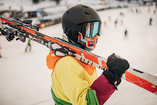 Female skier standing on a hill and carrying her skies on a snowcapped mountain ski resort.