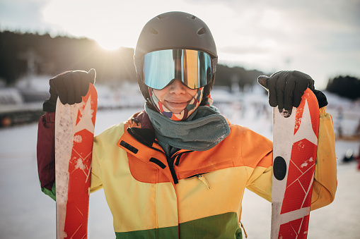 Portrait of a female skier standing on a hill and holding her skies on a snowcapped mountain ski resort.