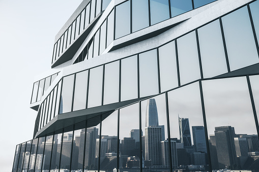 Side view on modern stylish business center building with panoramic windows reflecting the city skyline on light sky background. 3D rendering