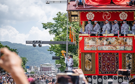 Kyoto, Japan - July 17, 2022: The float was led by two men in the front while the others were sitting at a high place playing instruments during Gion Matsuri Parade in Kyoto.