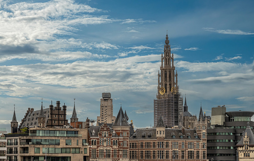Antwerpen, Flanders, Belgium - July 10, 2022: Seen from Scheld river. Skyline with 2 main towers: KBC bank, and Notre Dame Cathedral under blue cloudscape. Quay buildings up front