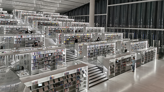 view into a wonderful modern library - ceiling, balcony, bookshelfs and corridors in warm colors