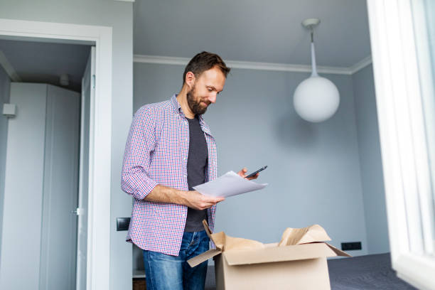 istock Young adult man opening package with clothes and using mobile 1427633689