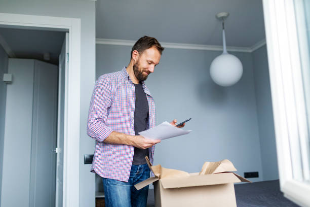 istock Young adult man opening package with clothes and using mobile 1427633758