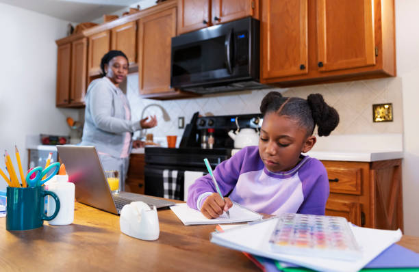 African-American girl studying, grandmother watching An African-American girl studying at home, doing her homework on a table in the kitchen. Her grandmother is out of focus in the background watching her. The granddaughter is almost 10 years old, an elementary student. grandmother real people front view head and shoulders stock pictures, royalty-free photos & images