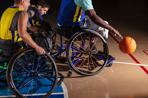 A cropped view of a wheelchair basketball player dribbling the ball, pursued by two other players. The African-American man is visible from his shoulders down. He is an amputee.