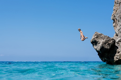 The boy is jumping from the rock into the water. Holidays in Corfu, Greece