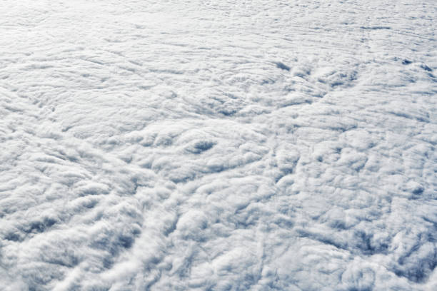 Over clouds top view from aircraft window, thick white blue clouds looks like soft foam, overcast with fresh frosty air. Beautiful cloudy sky view to troposphere, heavy cloudiness