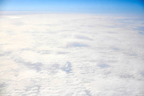 Breathtaking over clouds view from aircraft window, thick white blue clouds looks like soft foam, overcast with fresh frosty air. Beautiful cloudy sky view to troposphere, heavy cloudiness