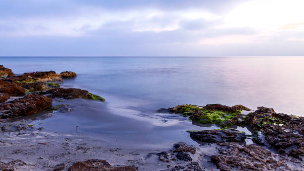istock Cloudy sunrise on a beach with sand and rocks 1427639845