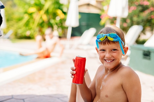 Happy boy is drinking a carbonated drink from a red can in the pool. Happy holidays Corfu, Greece
