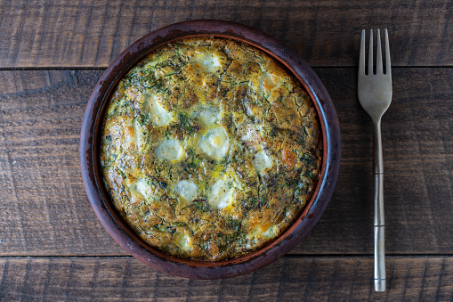 Ceramic bowl with vegetable frittata, simple vegetarian food. Frittata with eggs, green beet leaves, onion, pepper, spices and cheese on wooden table, close up. Italian egg omelette, top view