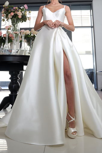Woman dressed in her wedding gown sitting on a chair at a hotel with her skirt moved to see her shoes. She is reaching down to fasten one.