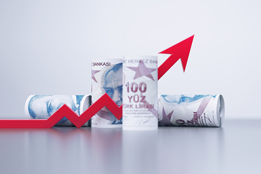 Rolled up 100 Turkish Lira bills and red arrow symbol sitting on gray background. Horizontal composition with copy space. Finance concept.