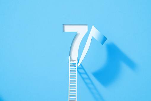 White ladder leaning onto blue number seven which folds on white background. Horizontal composition with copy space.