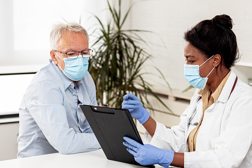 African american woman doctor in ambulance and male senior  in a medical clinic wearing protective face masks to avoid the transfer of viruses