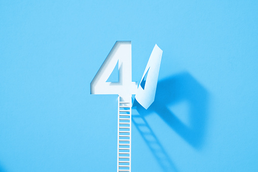 White ladder leaning onto blue number four which folds on white background. Horizontal composition with copy space.