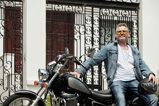 Pensive mature man leaning on motorcycle when waiting for girlfriend outside