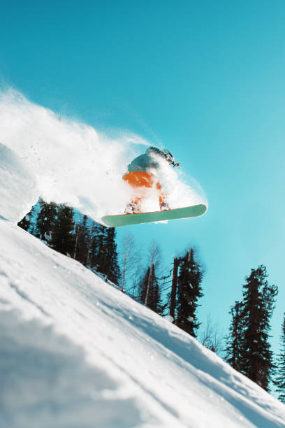 istock Snowboarder jumps from a high snow-covered springboard in a forest against a blue sky 1427658121