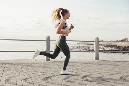 Full length of sporty caucasian young woman jogging on promenade against sea and sky during sunny day