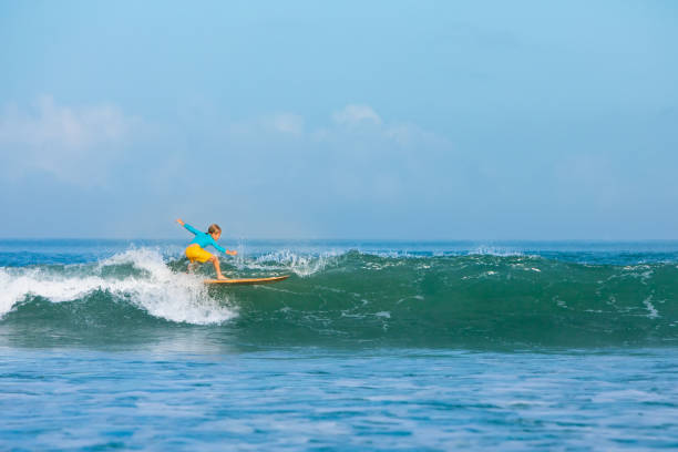 Happy surf boy - young surfer learn to ride on surfboard with fun on sea waves. Active family lifestyle, kids outdoor water sport lessons, swimming activity in surfing camp. Summer vacation with child