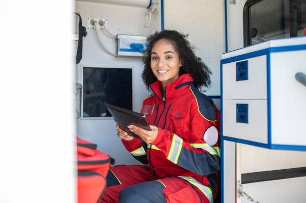 Paramedic posing for the camera in the medical emergency vehicle Cheerful female doctor with the tablet computer in her hands sitting in the ambulance car medic stock pictures, royalty-free photos & images