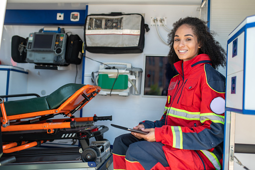 Smiling happy paramedic with the tablet in her hands sitting in the medical emergency vehicle