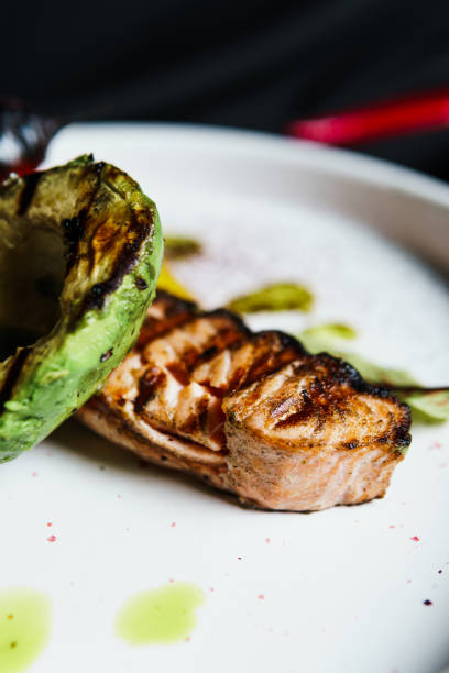 Grilled salmon fish fillet with vegetables and avocado on the plate, close up