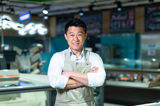 Portrait of Asian salesman in seafood and fish shop man smiling with arms crossed and looking at camera